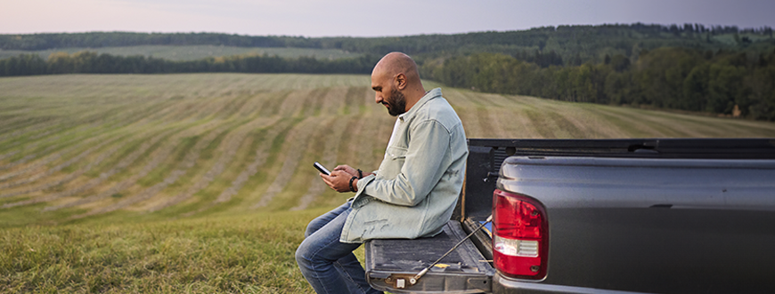 decorative image, man sitting on his truck bed looking at a phone