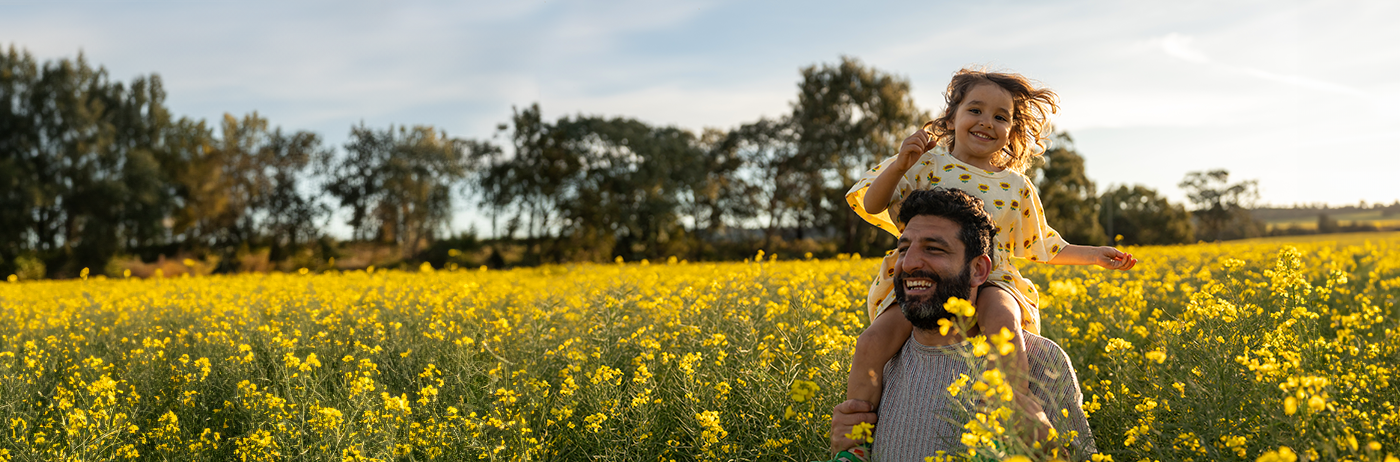 man walking through a field with his daughter on his shoulders